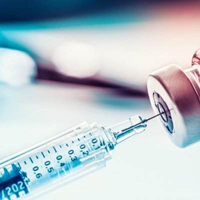 Syringe needle tip going into container of vaccine with blurred background